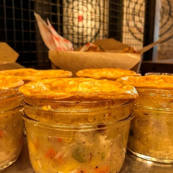 Golden-crusted pot pies in glass jars, filled with creamy chicken and vegetables, on a metal tray.