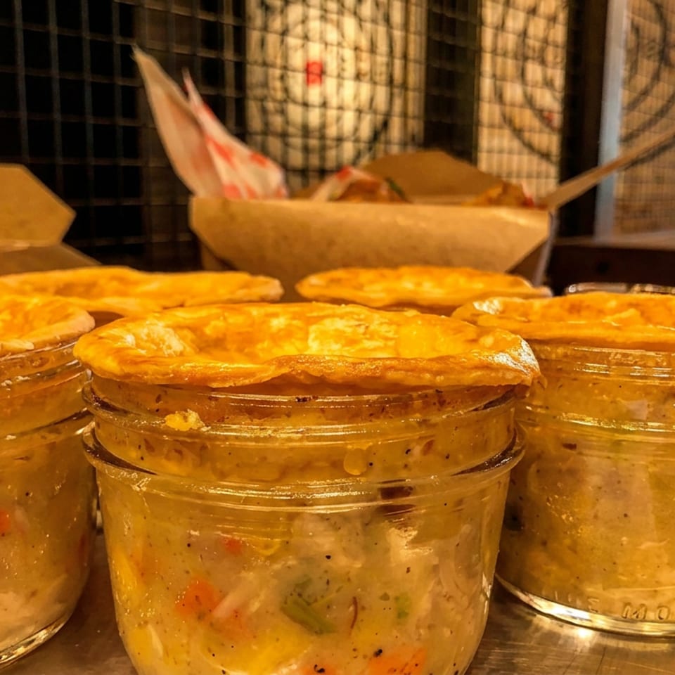 Golden-crusted pot pies in glass jars, filled with creamy chicken and vegetables, on a metal tray.