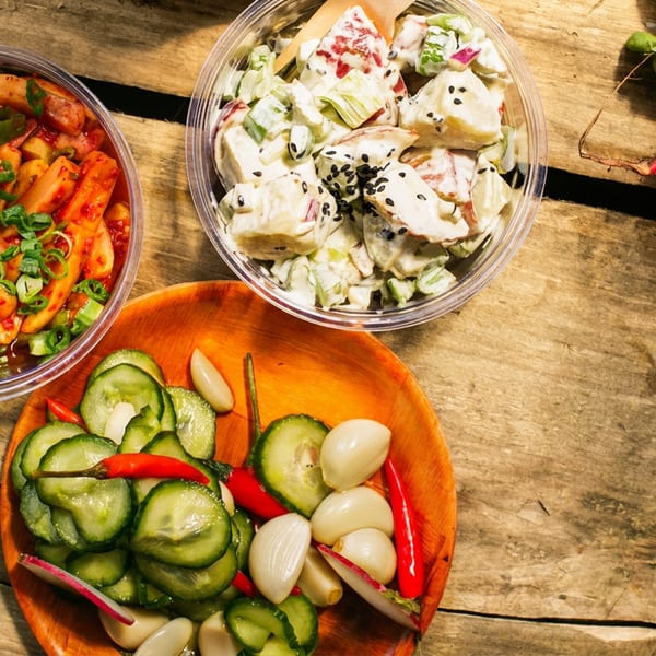 Three bowls of Korean side dishes and fresh radishes on a rustic wooden surface.
