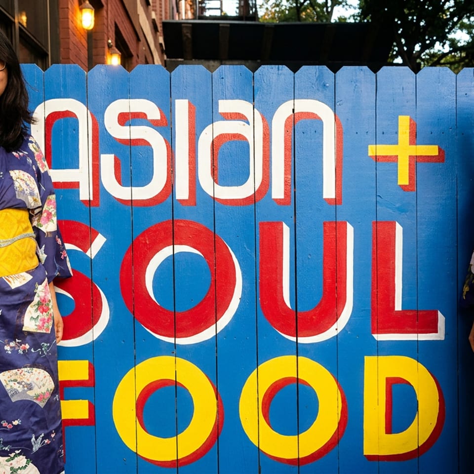 Two smiling women in traditional kimonos pose next to a vibrant "ASIAN + SOUL FOOD" sign.