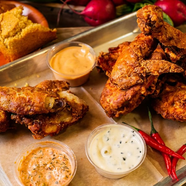 Golden fried chicken, cornbread, and three sauces on a metal tray with red peppers.