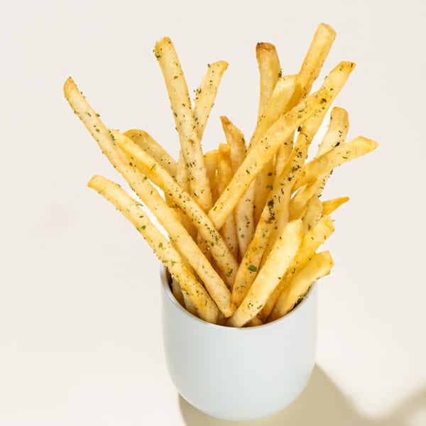 Golden french fries seasoned with herbs, served upright in a light blue cup on a white surface.