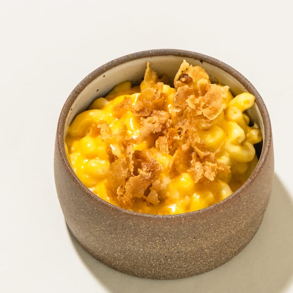 Creamy mac and cheese topped with crispy fried onions in a rustic bowl on a white surface.