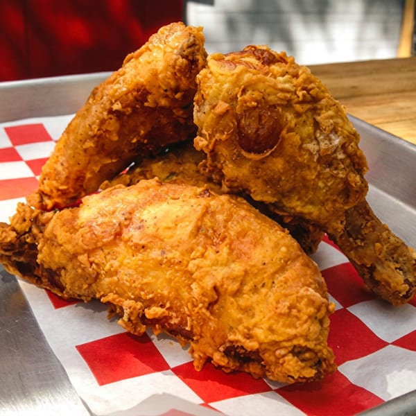 Golden-brown fried chicken pieces on a metal tray with red and white checkered paper.