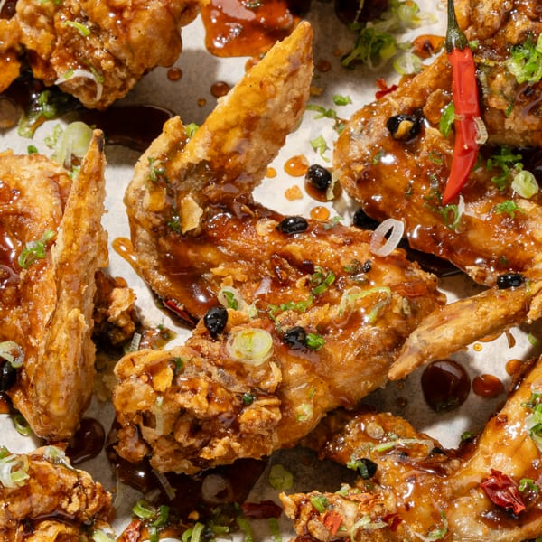 Crispy fried chicken wings coated in a glossy brown sauce, garnished with green onions and red chilies.
