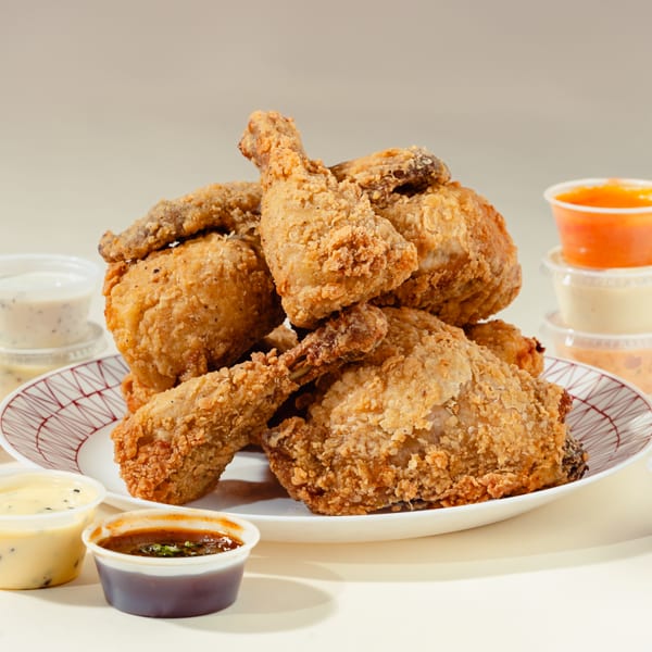 Crispy fried chicken pieces piled on a white plate, surrounded by various dipping sauces.
