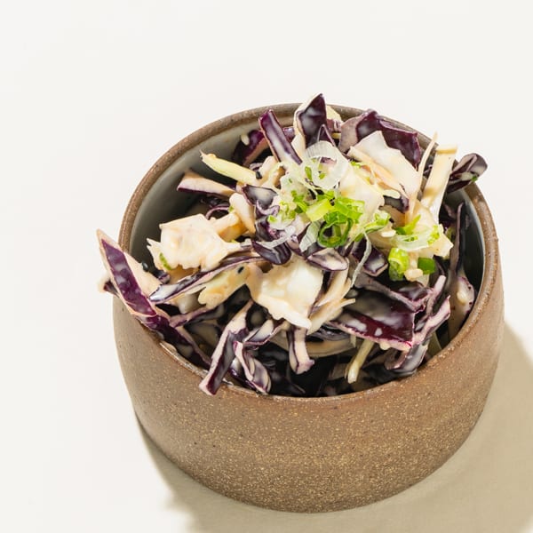 Creamy coleslaw with shredded red cabbage, green onions, and white cabbage in a brown bowl.