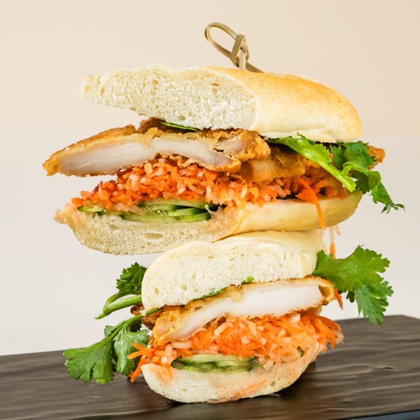 A stacked banh mi sandwich with fried chicken, pickled carrots, cucumbers, and cilantro on a baguette.