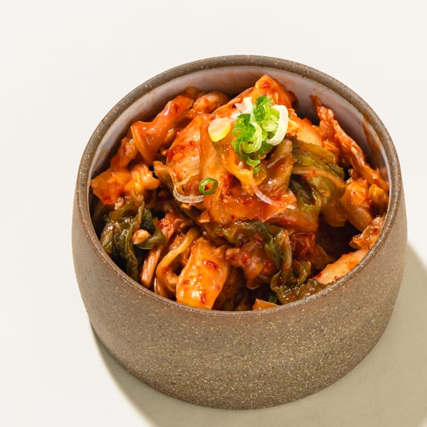 A bowl of spicy kimchi, garnished with sliced green onions, on a white surface.