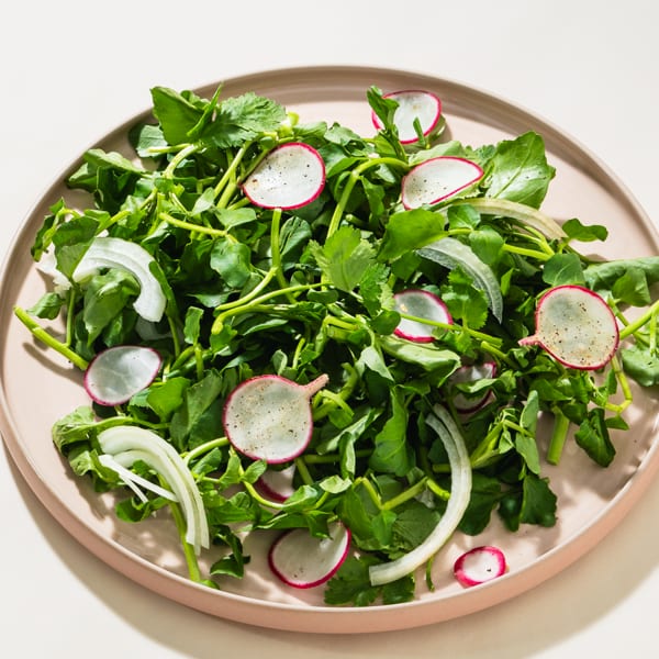 Fresh green salad with sliced radishes and white onions on a light pink plate.